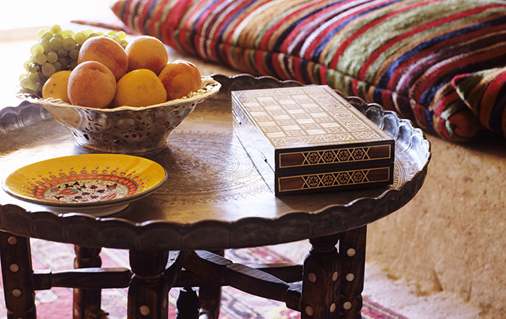 Fruit bowl on Oriental side table in front of striped cushions on platform